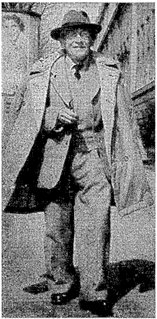 Photo von gehendem und lächelndem Erwin Schrödinger in Anzug und darübergelegtem Mantel.
